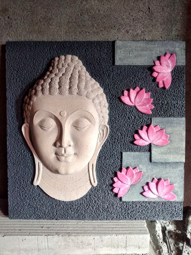 Sculpted Buddha face wall relief with pink lotus flowers on a dark textured panel