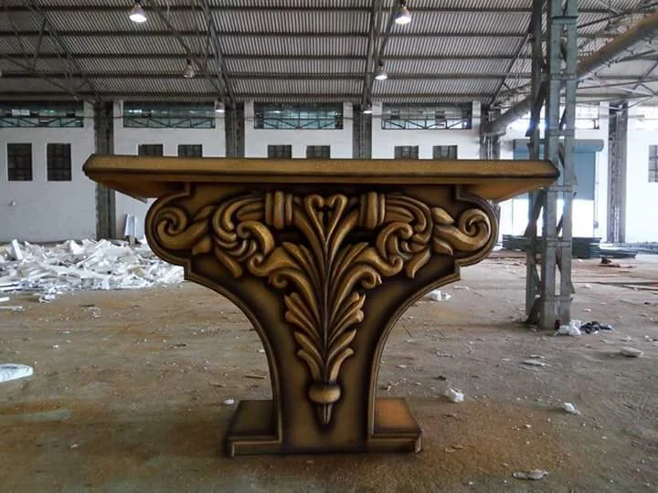 Ornate gold and brown sculpted pedestal in a fabrication workshop